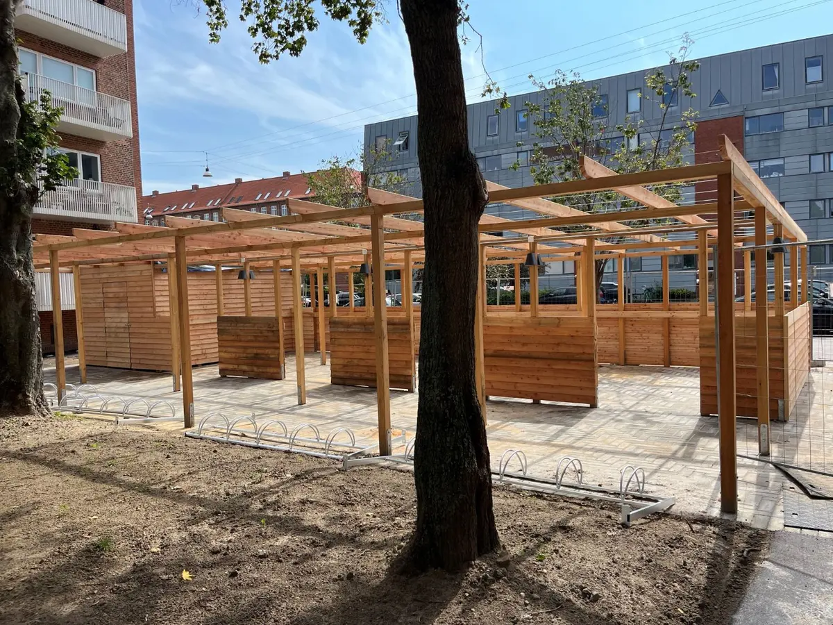 Gårdmiljø i træ med pergola, cykelstativer og skure mellem etageboliger