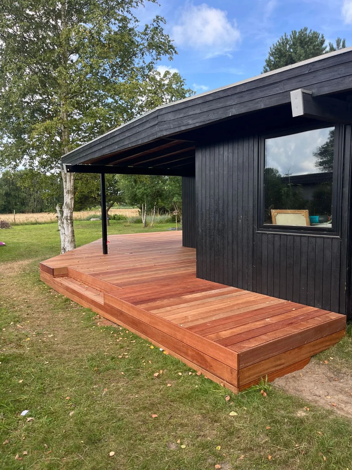 Hjørnet af en hævet jatoba-terrasse under husets tagudhæng i Liseleje, med kanten klædt i samme træ.