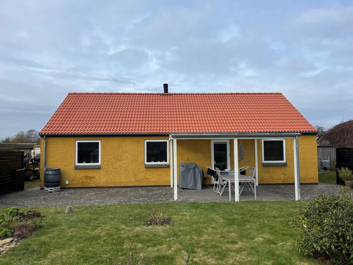 Nyt rødt tag på et gult hus med overdækket terrasse