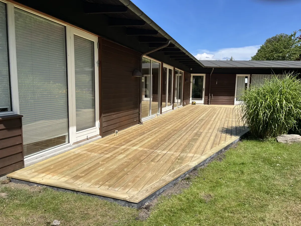 Terrasse i trykimprægneret træ langs et hus med store vinduespartier